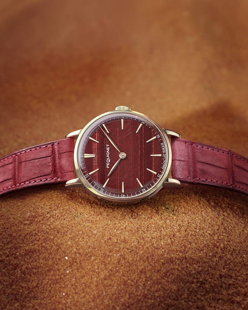 Pequignet Attitude Tiger’s Eye Limited Edition watch with a red leather strap on some orange material 